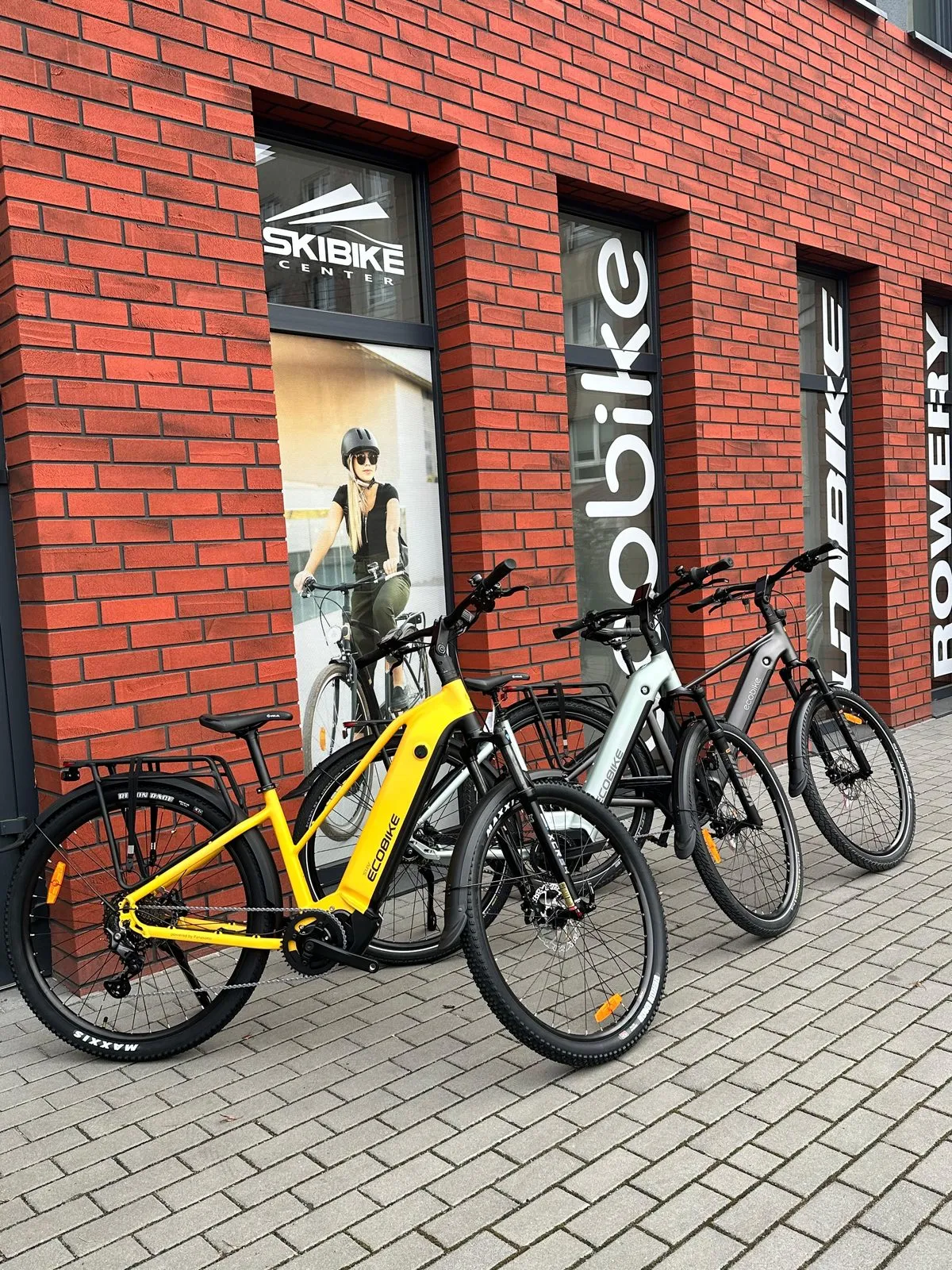 Trzy rowery elektryczne Ecobike, w tym żółty, ustawione przed witryną salonu Skibike Center